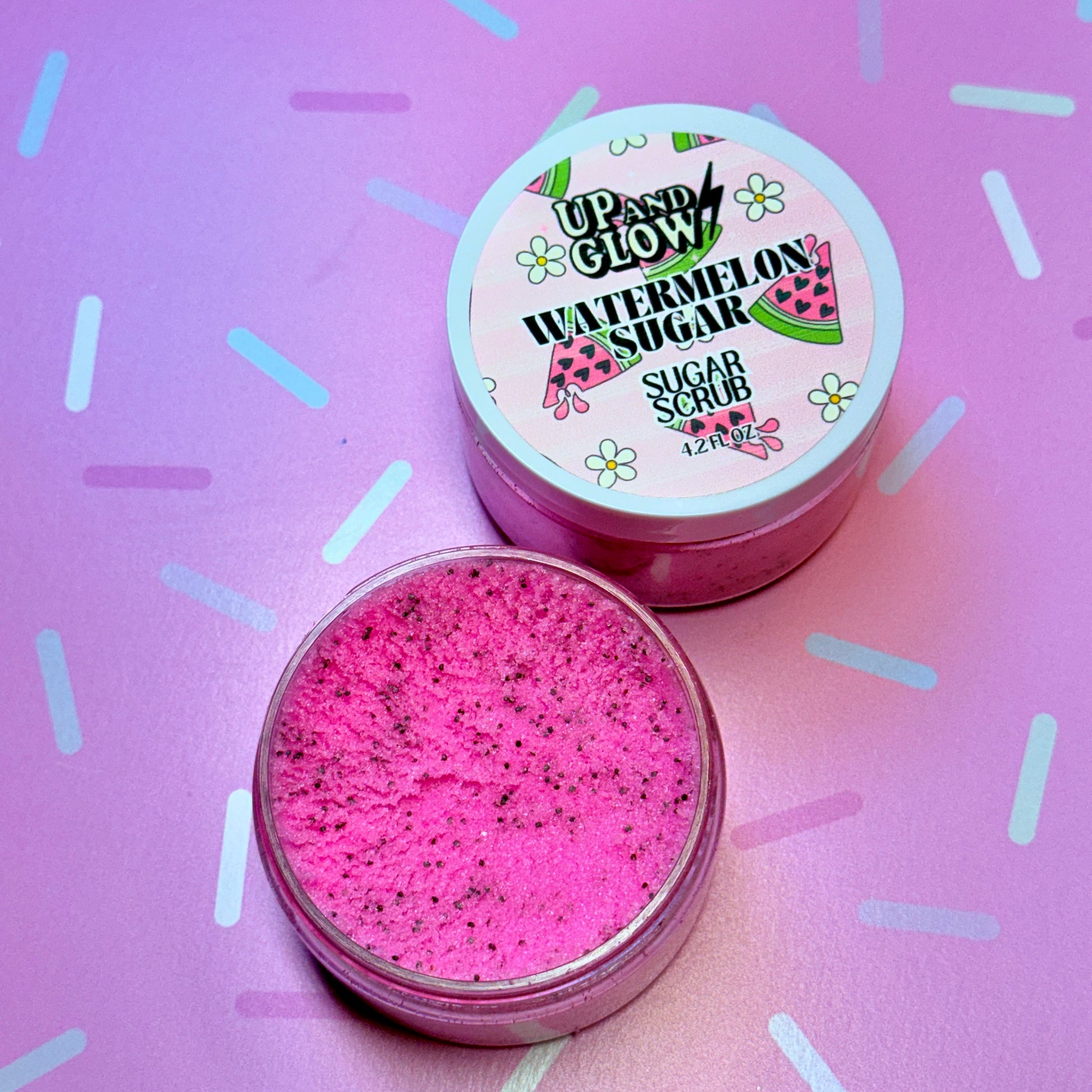 Pink sugar scrub with a labeled container on a pink background