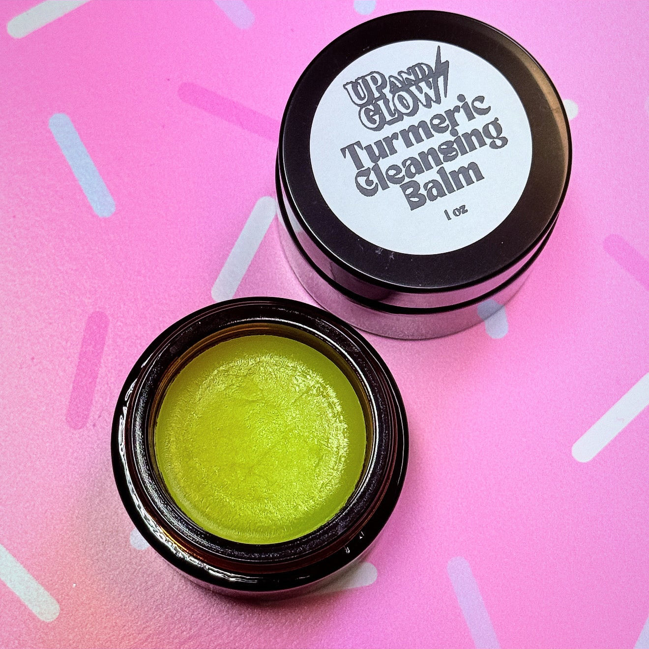 Turmeric cleansing balm in a black container on a pink background