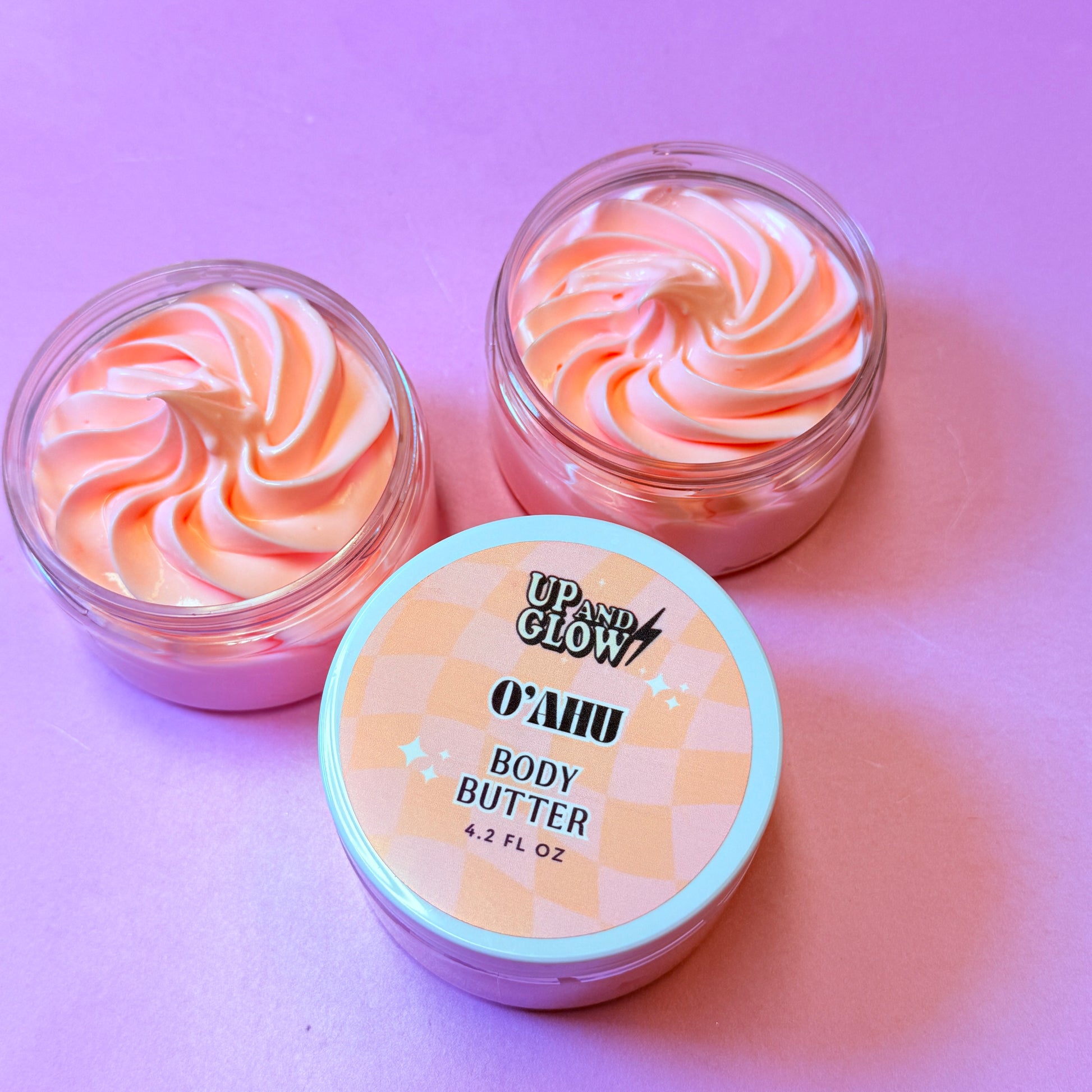 Two containers of Oahu body butter with a pink swirl on a pink background