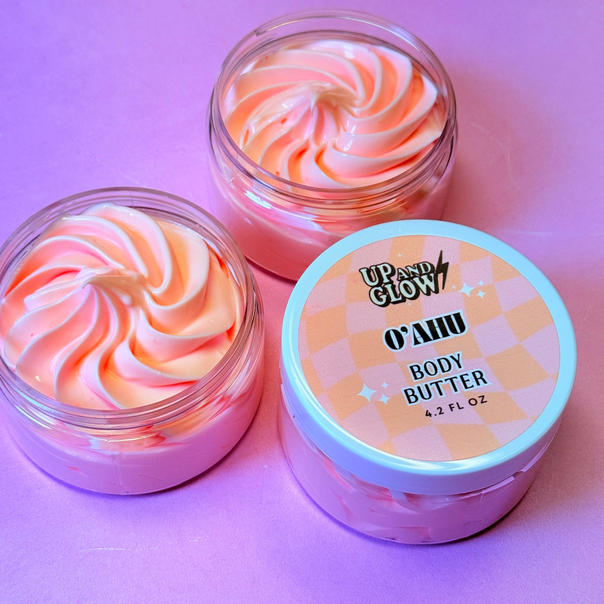 Two containers of swirled body butter with a labeled container on a pink background