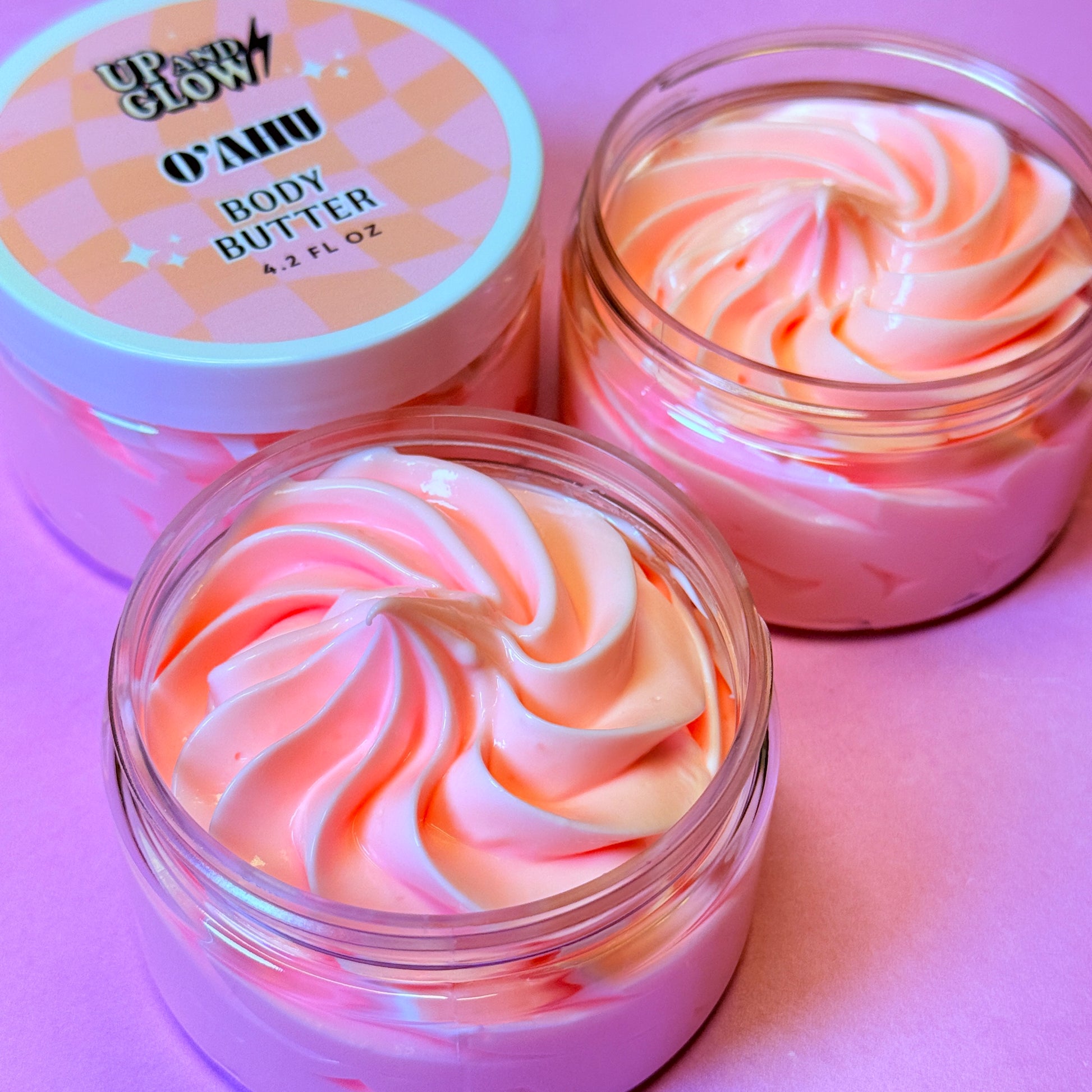 Two jars of pink and white swirled body butter with a visible brand label on a pink background.