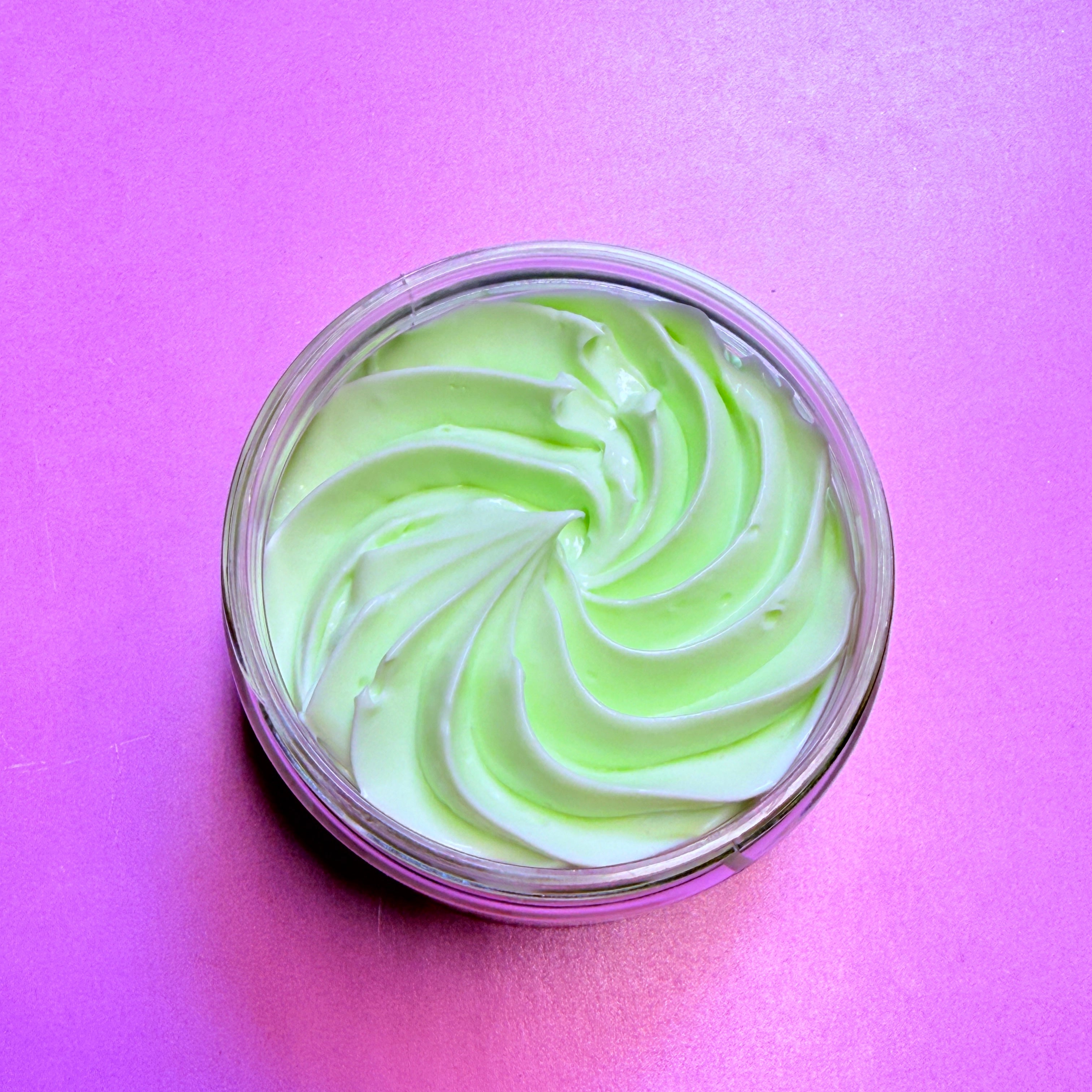Jar of green and white swirled cream on a pink background. Body Butter for deep hydration and repair