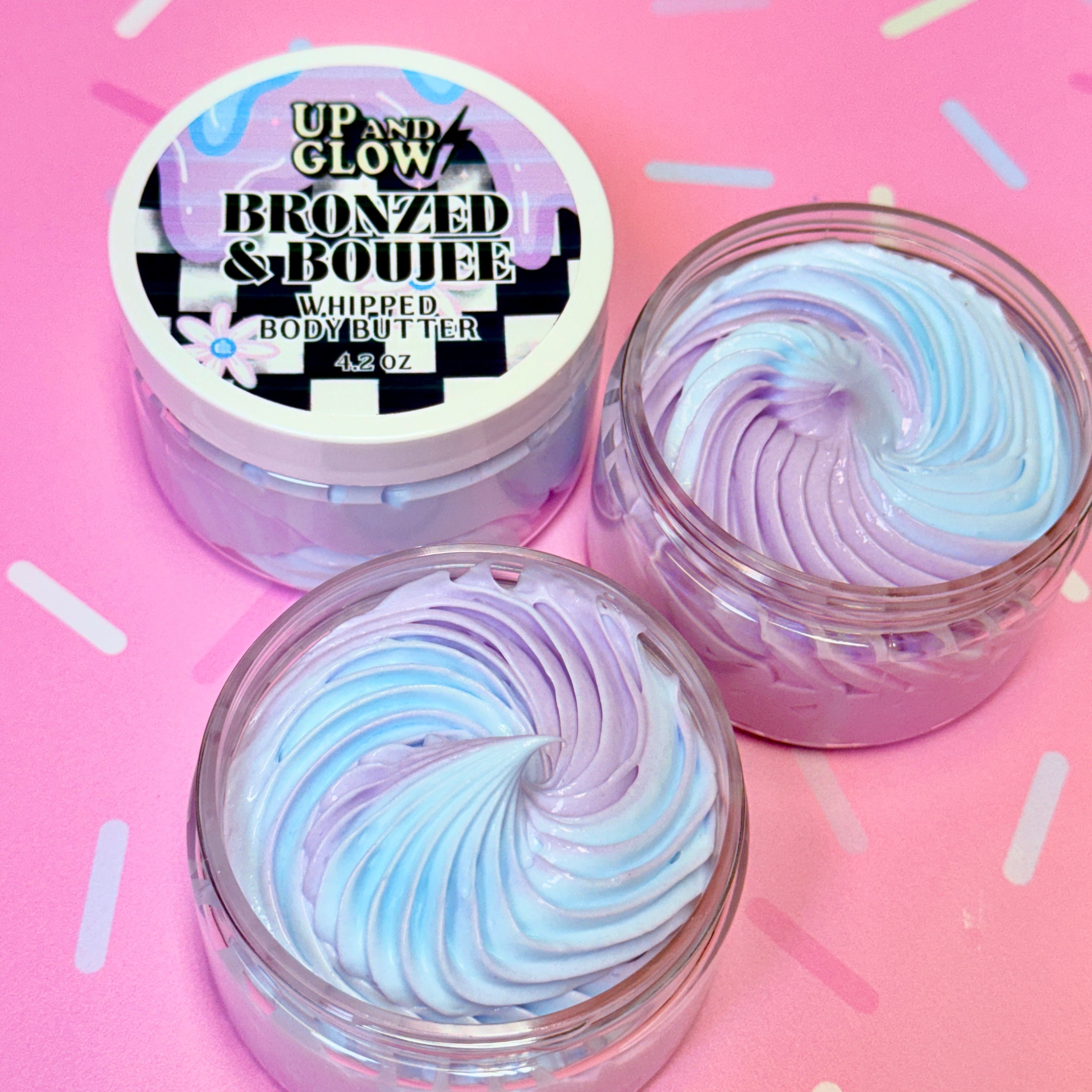 Two containers of 'Up and Glow Bronzed & Boujee Whipped Body Butter' on a pink background.