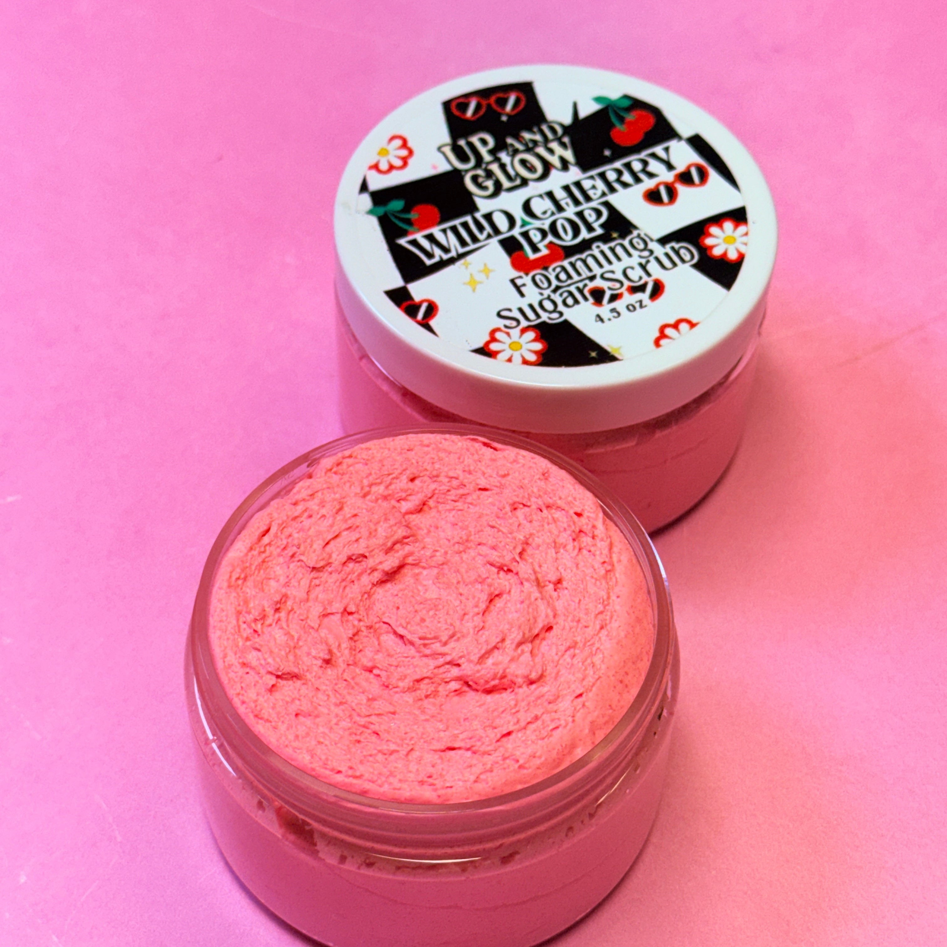 Pink foaming sugar scrub in a jar with a labeled lid on a pink background